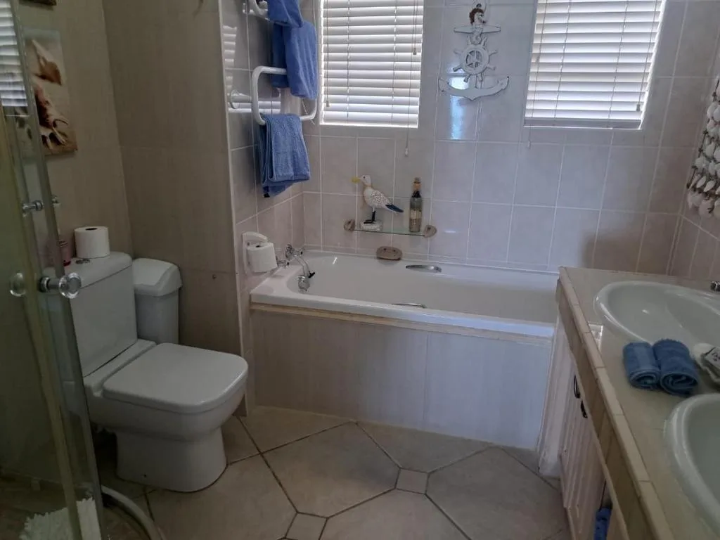 Bright bathroom with bathtub, toilet, dual sinks and coastal decor