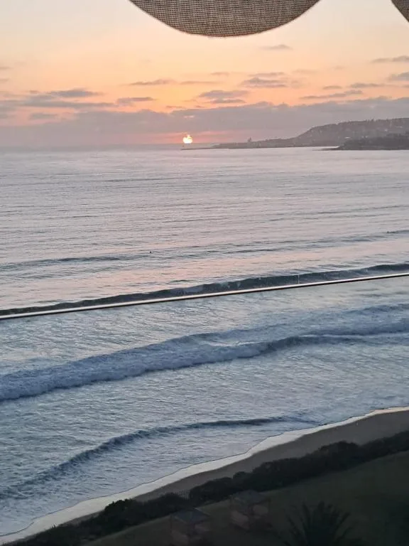 Sunset over ocean with waves, mountains visible on horizon from deck