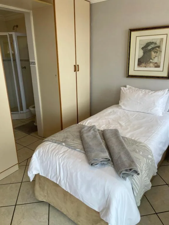 Single bed with white linens and folded gray towels, wardrobe and wall art