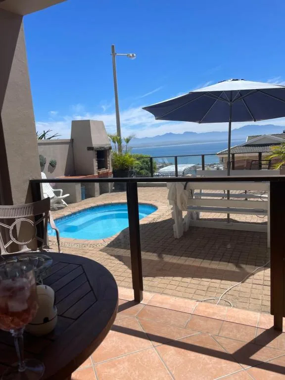 Outdoor patio with pool, umbrella, and ocean view beyond railing