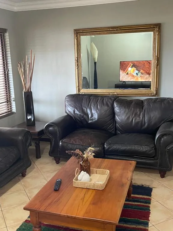 Living room with black leather sofa, wooden coffee table, and gold-framed mirror