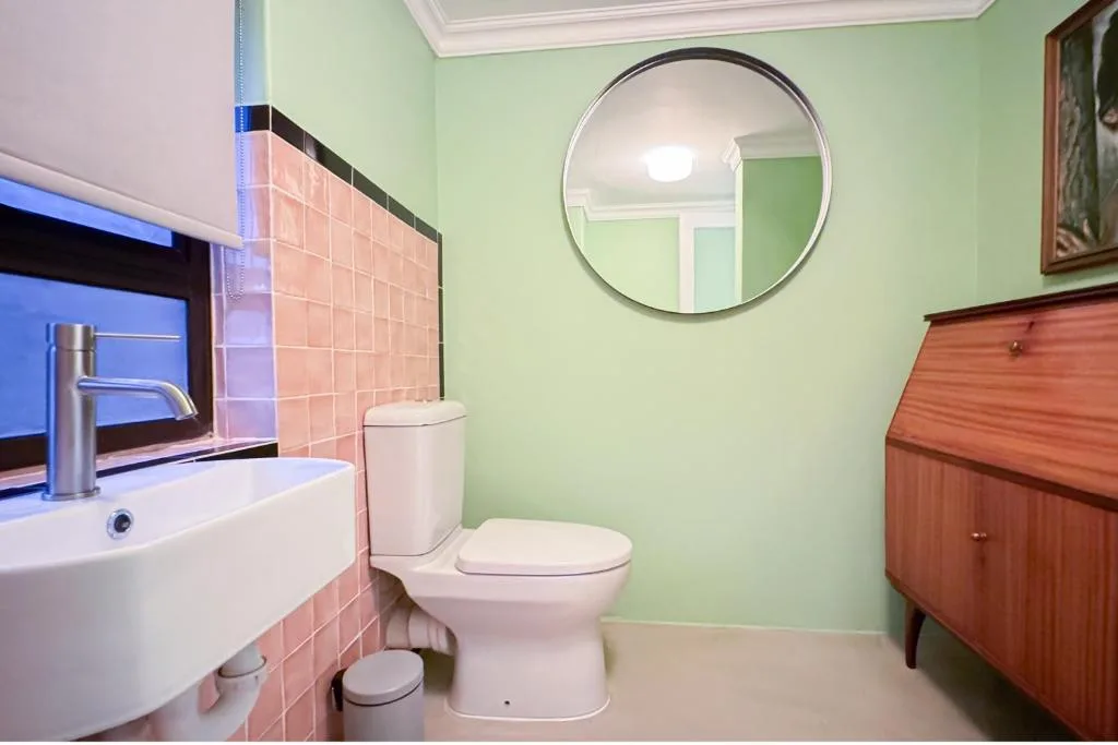 Modern bathroom with mint green walls, round mirror, and pink tile accents