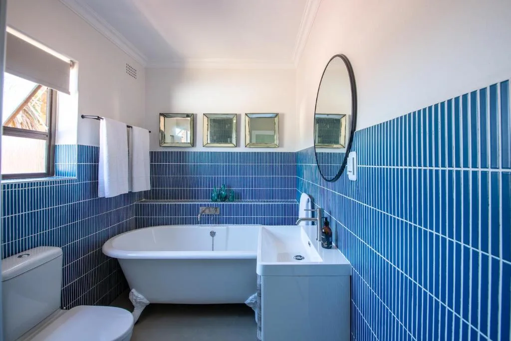 Modern bathroom with blue tile walls, freestanding bath, and round mirror