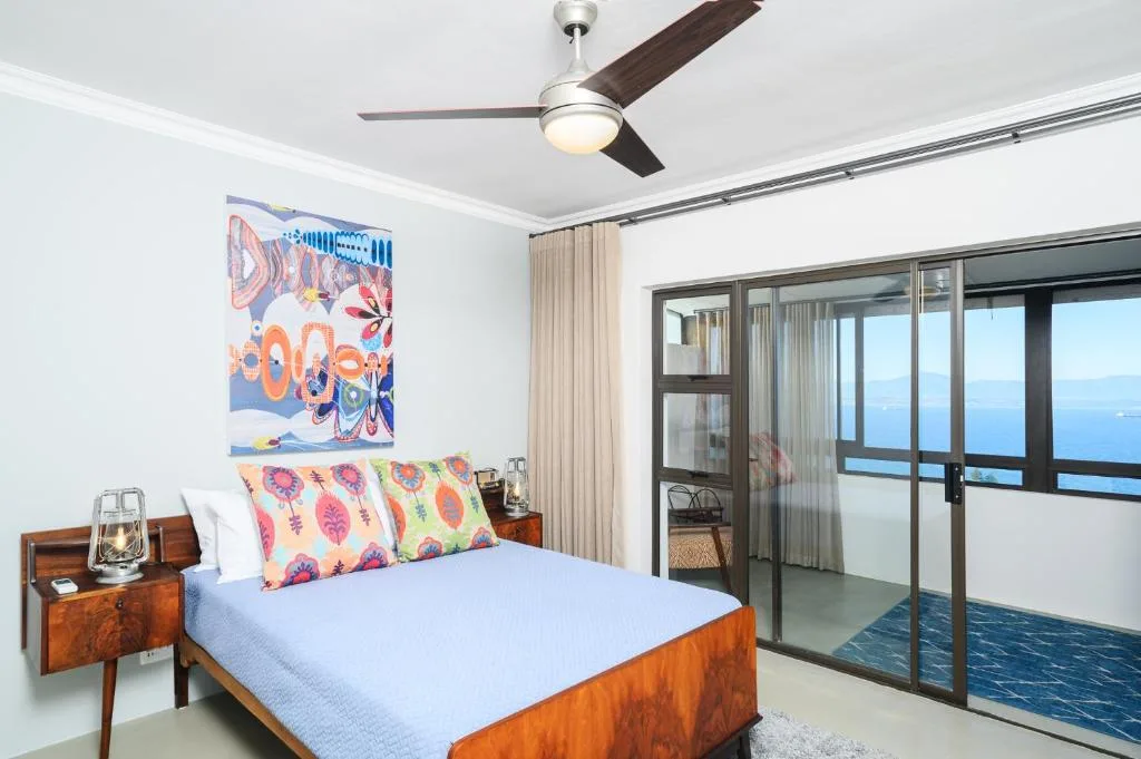 Bright bedroom with wooden bed, colorful pillows, ocean view through glass doors