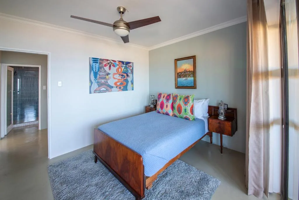 Spacious bedroom with wooden bed, blue bedding, colorful cushions, and artwork