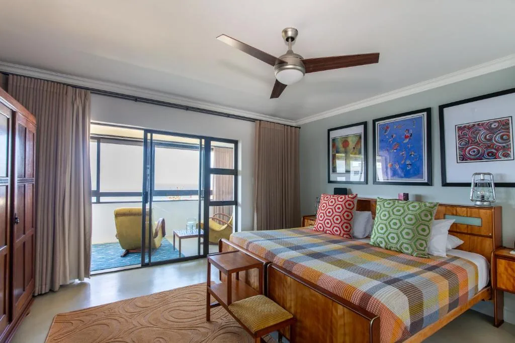 Bright bedroom with queen bed, colorful pillows, and ocean view through glass doors