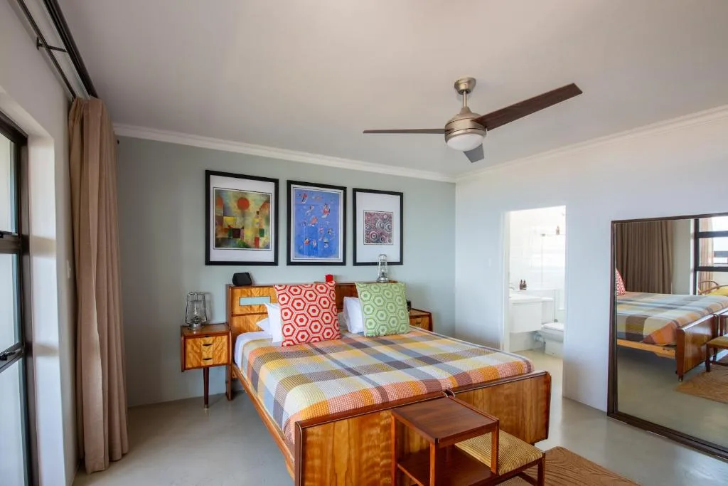Bright bedroom with wooden bed, colorful cushions, ceiling fan, and artwork