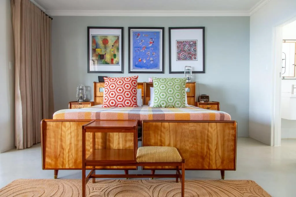 Spacious bedroom with wooden bed frame, colorful pillows, and framed artwork on pale blue wall