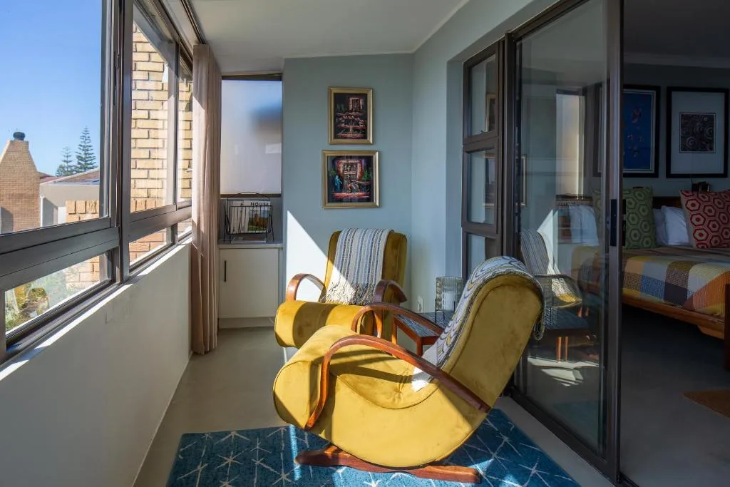 Sunny balcony with yellow armchairs, coastal views, and framed artwork