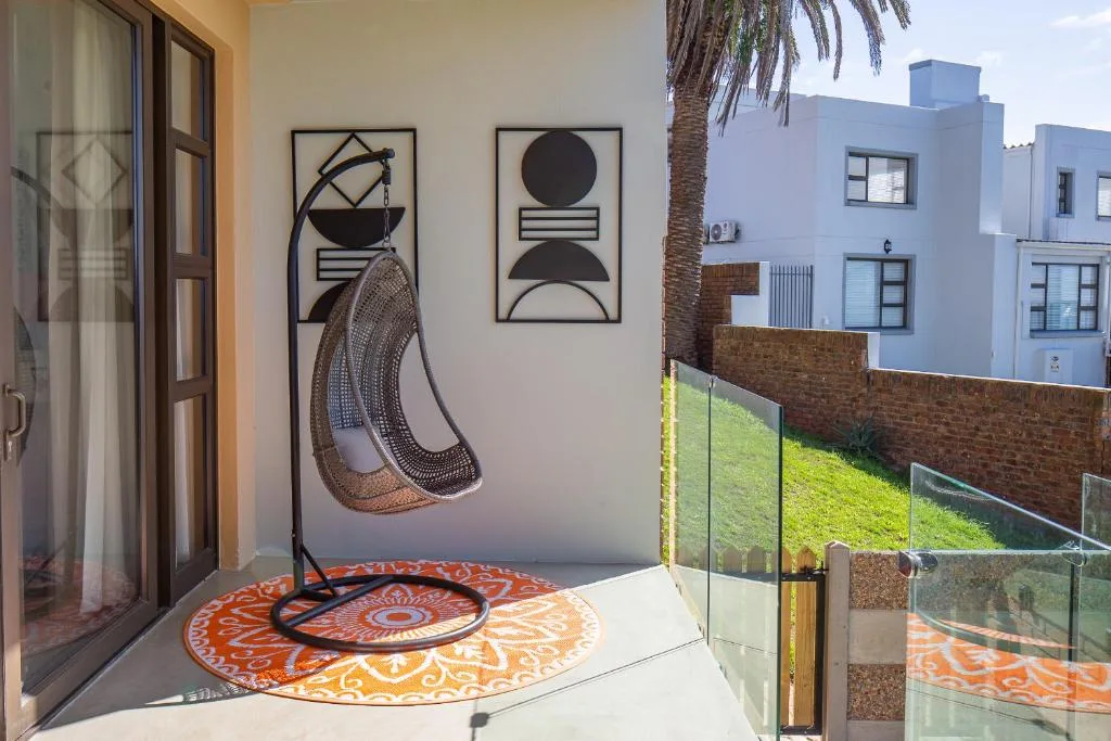 Modern patio with hanging chair, abstract wall art, and glass railing overlooking garden