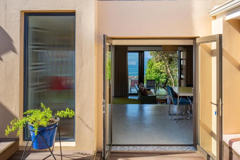Open sliding doors leading to furnished deck with ocean view beyond