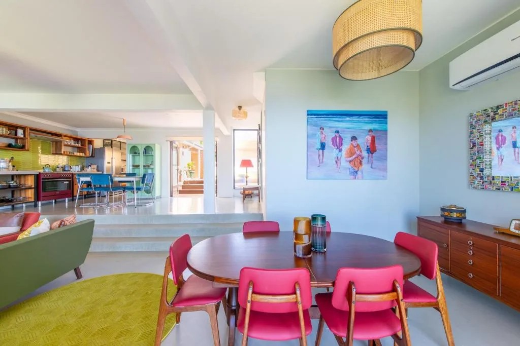 Modern dining area with round table and vibrant pink chairs, open-plan kitchen visible