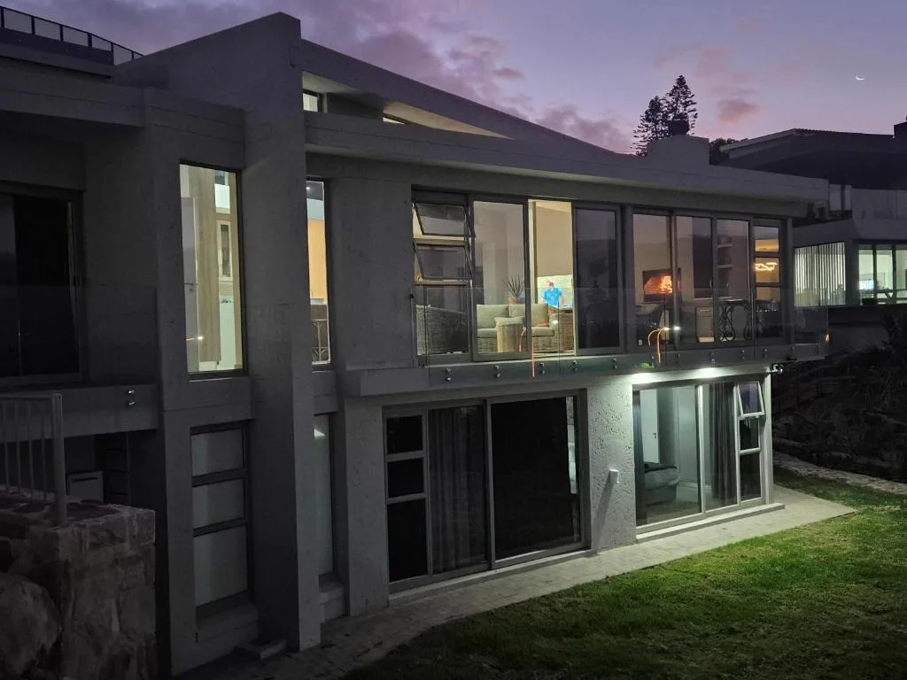 Modern dark-clad villa exterior at dusk with illuminated windows and manicured lawn