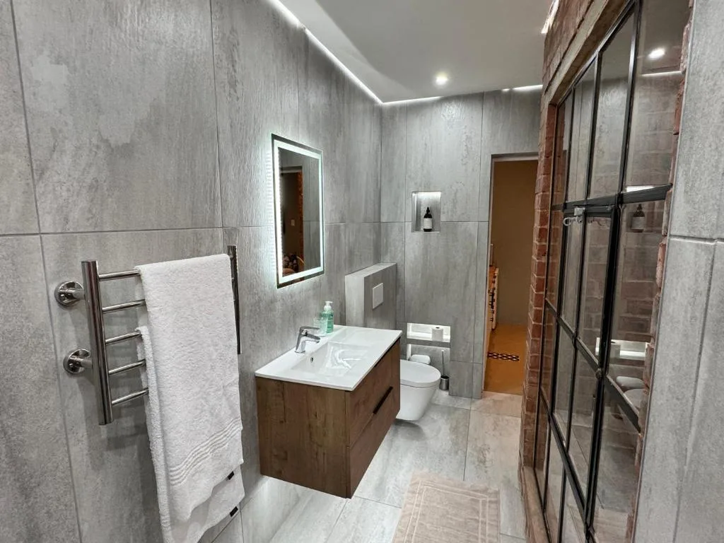 Modern bathroom with gray tile walls, wooden vanity, and walk-in shower