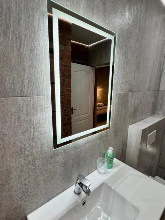 Modern bathroom with illuminated mirror, white sink, and gray tile walls