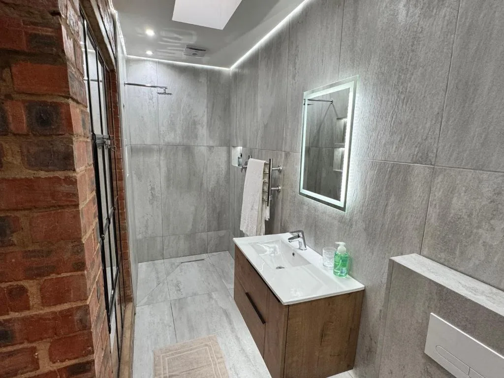 Modern bathroom with gray tiled walls, walk-in shower, and wooden vanity sink