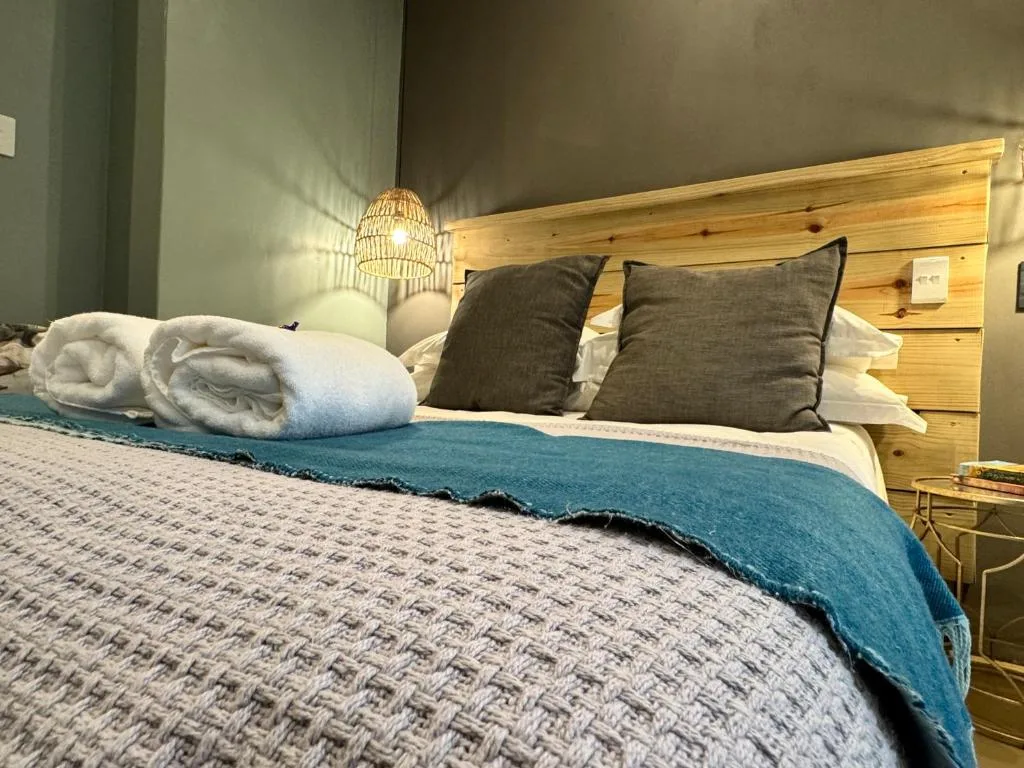 Comfortable bed with pillows, blue throw, and rolled towels provided