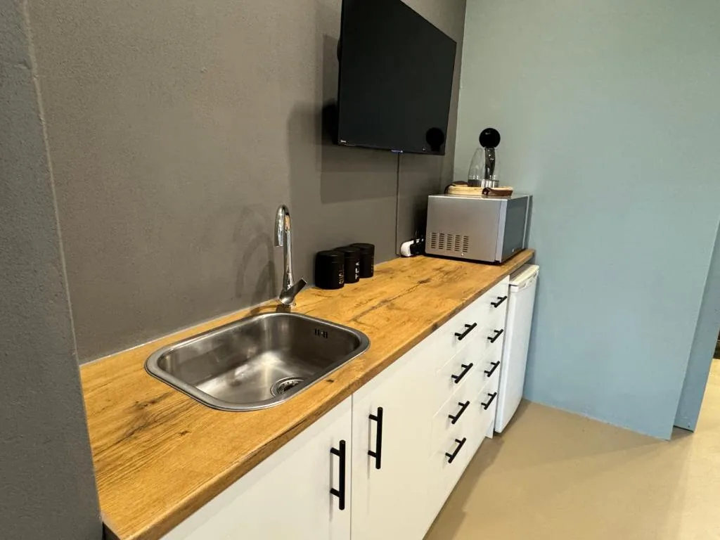 Compact kitchenette with stainless sink, wooden countertop, white cabinetry, and wall-mounted TV
