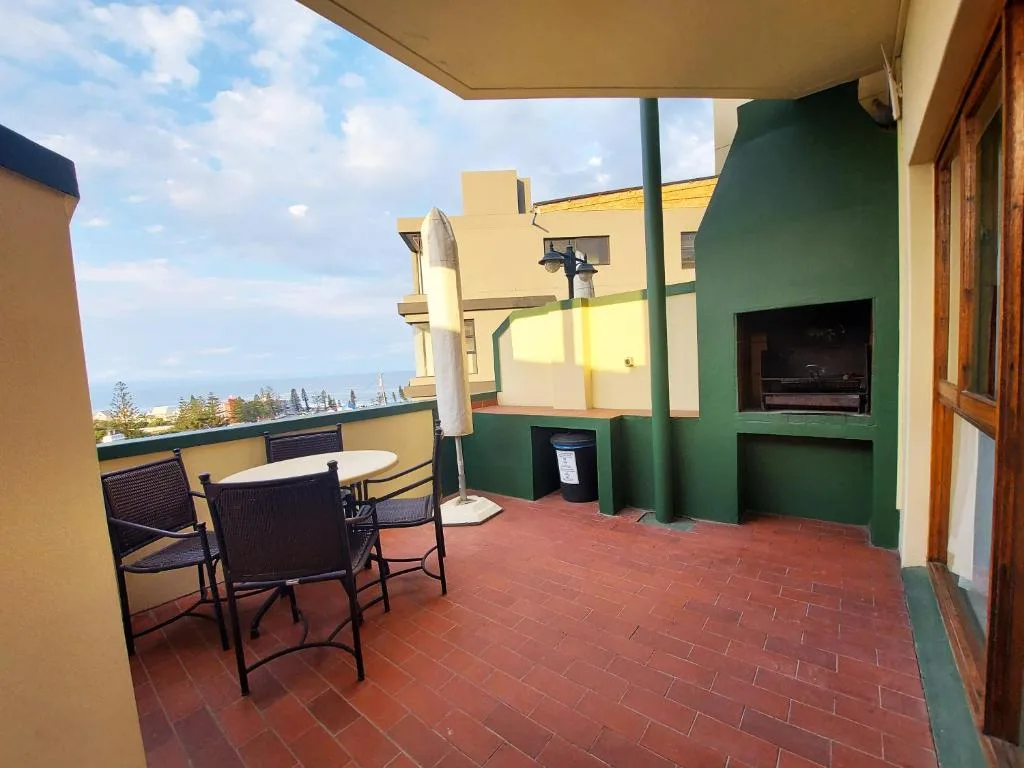 Shaded outdoor deck with dining table, chairs, and ocean view beyond