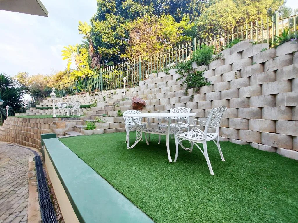Outdoor patio with white furniture on artificial grass and stone walls
