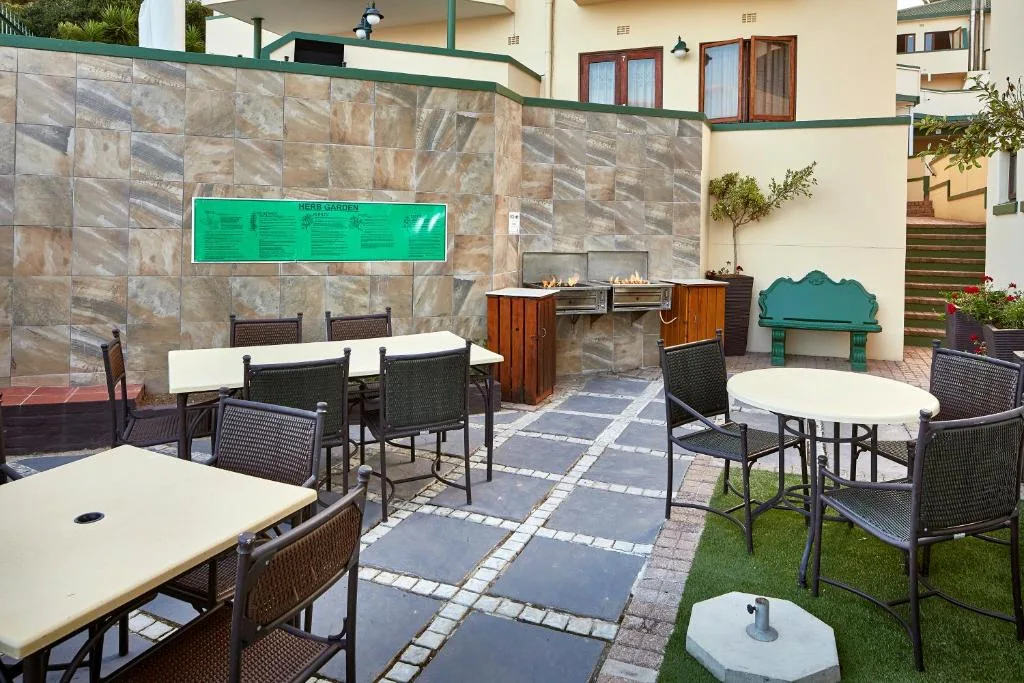 Outdoor patio with dining tables, chairs, and braai area against stone wall