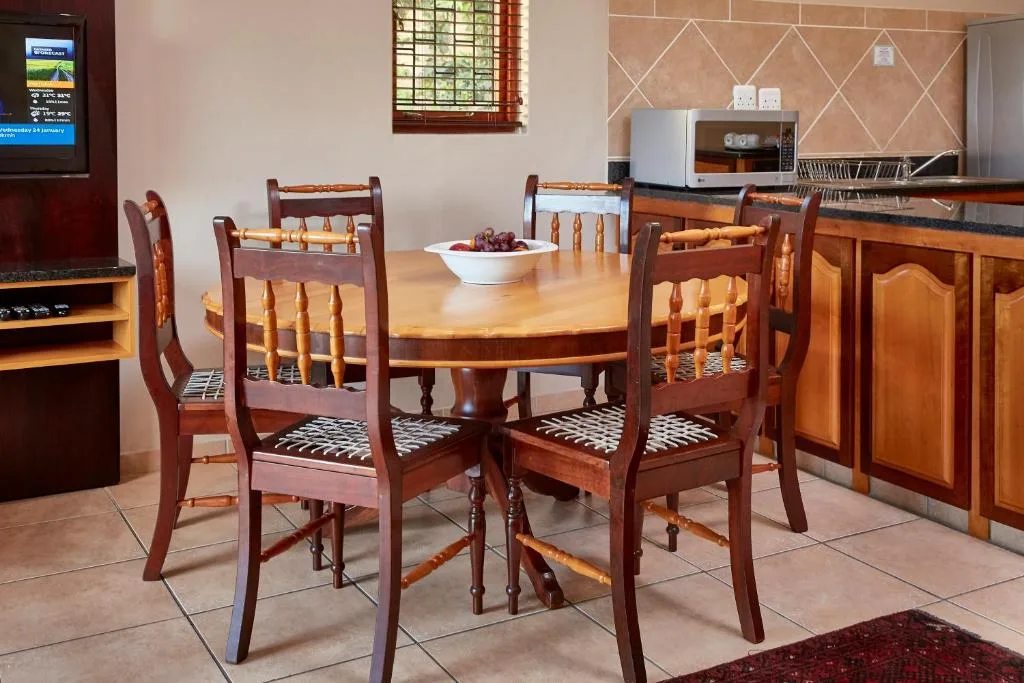 Wooden dining table with four chairs and kitchen area visible