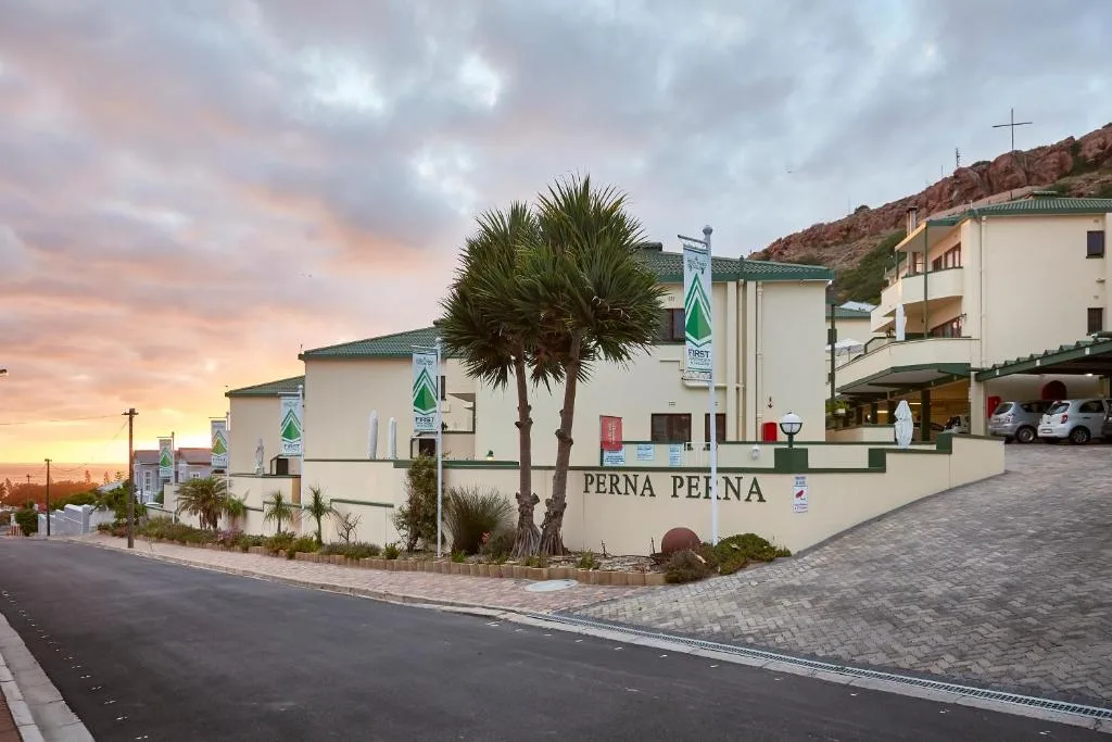 Modern accommodation complex with white buildings, palm trees, and sunset sky