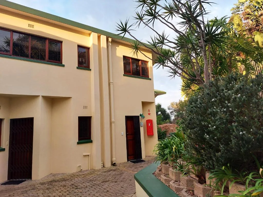 Cream-coloured apartment building with green trim and red doors, tropical landscaping