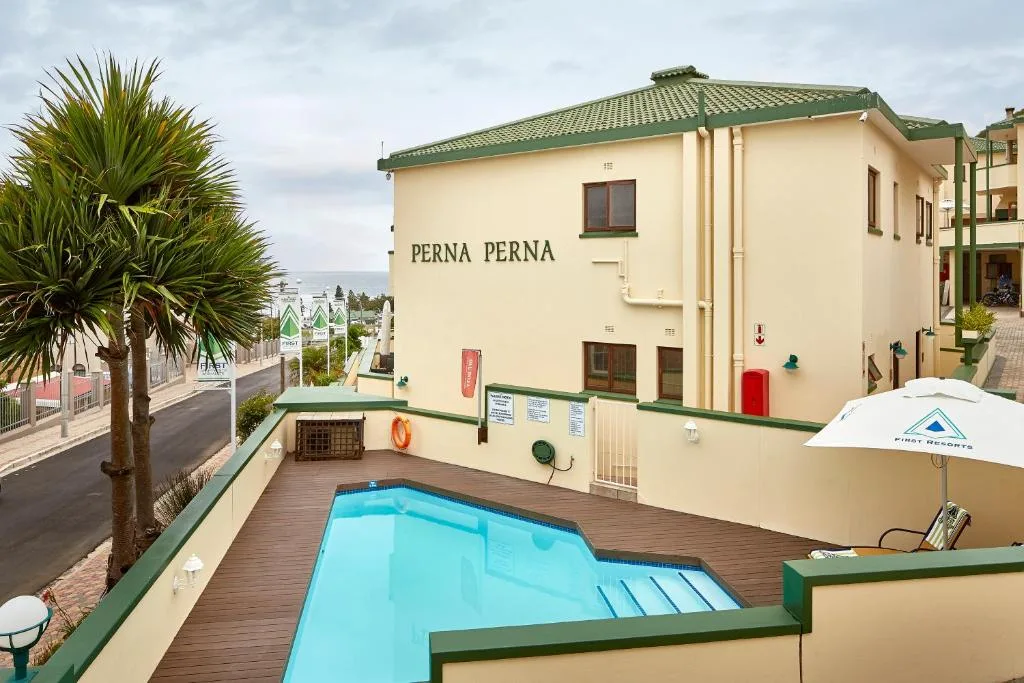 Bright turquoise swimming pool on wooden deck with cream building and palm trees