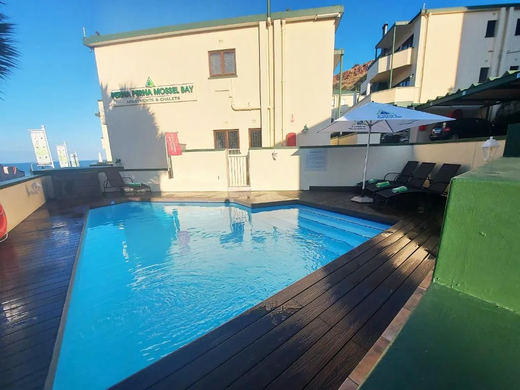 Bright blue swimming pool with wooden deck and lounge chairs overlooking ocean