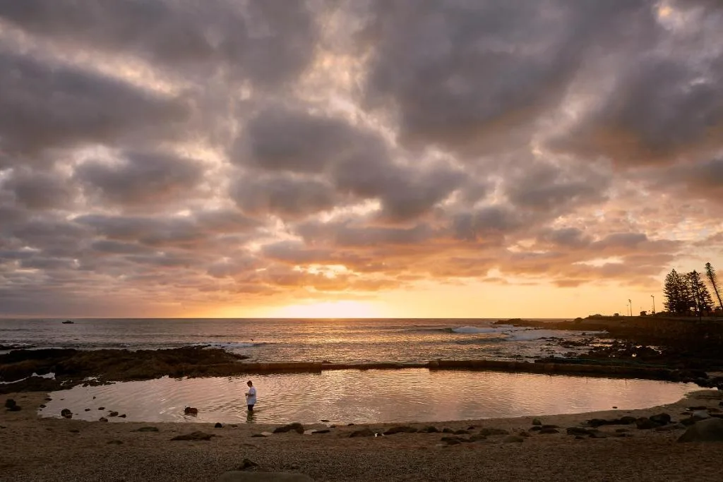 Sunset over ocean with tidal pool and person wading, dramatic sky