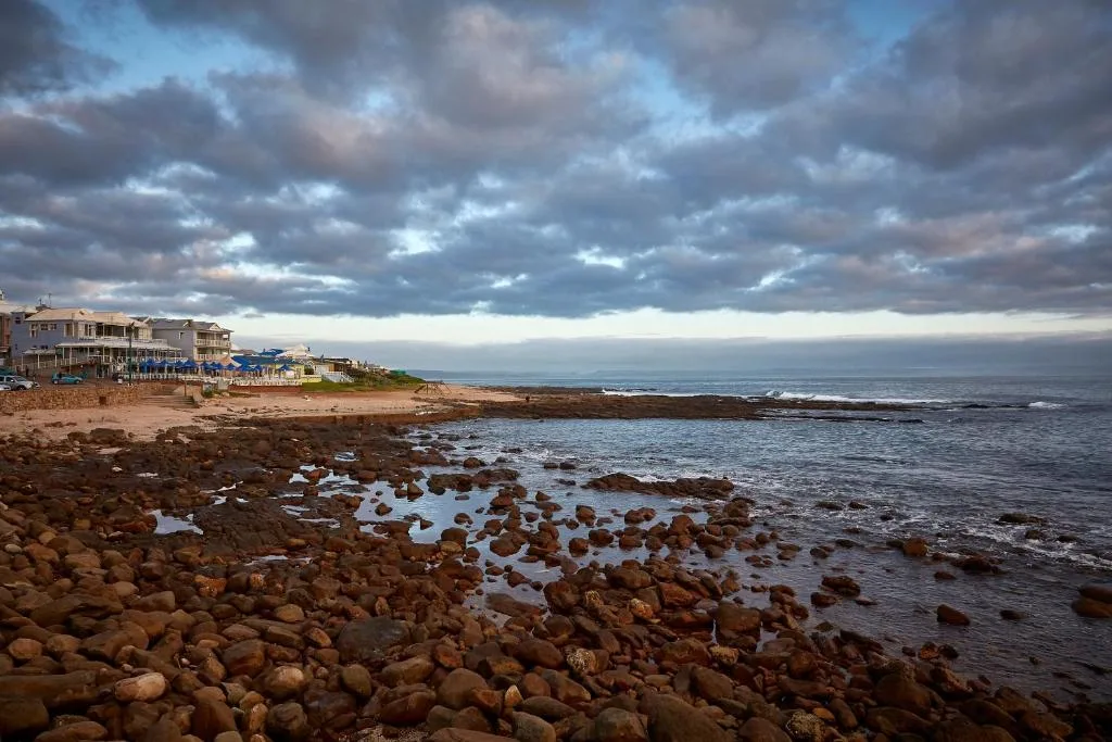 Dramatic ocean view with rocky coastline and beachfront properties under cloudy sky