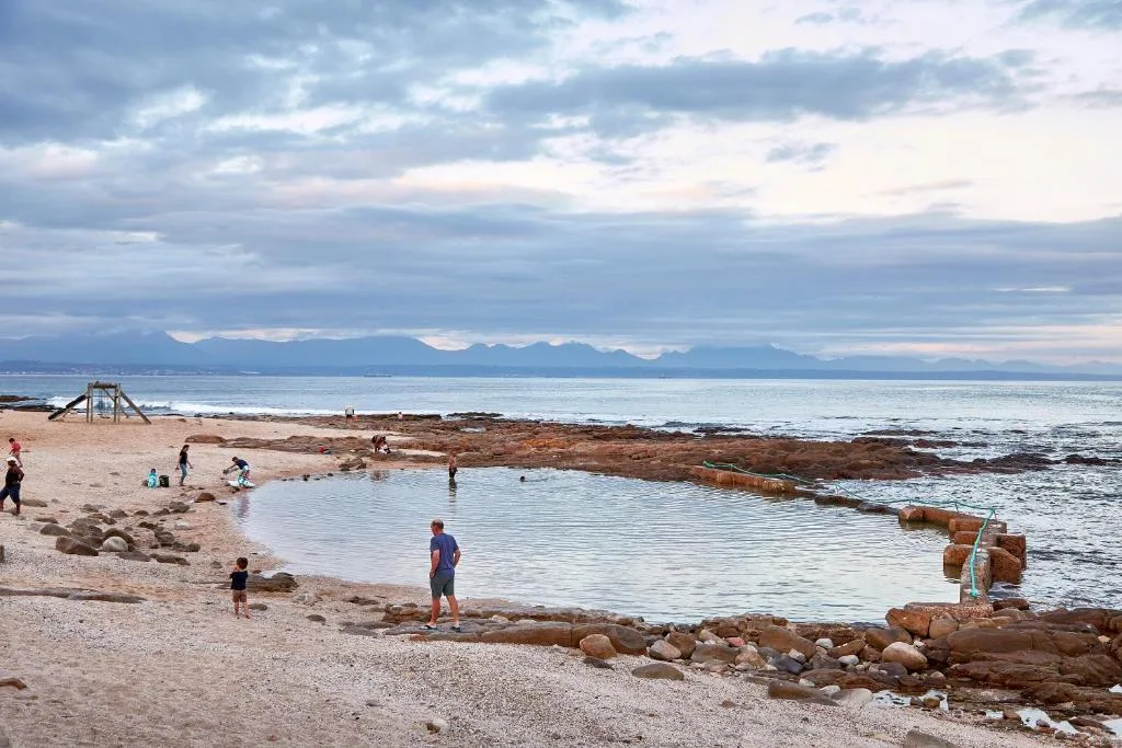 Scenic coastal view with mountains, beach, tidal pool, and visitors enjoying the shoreline
