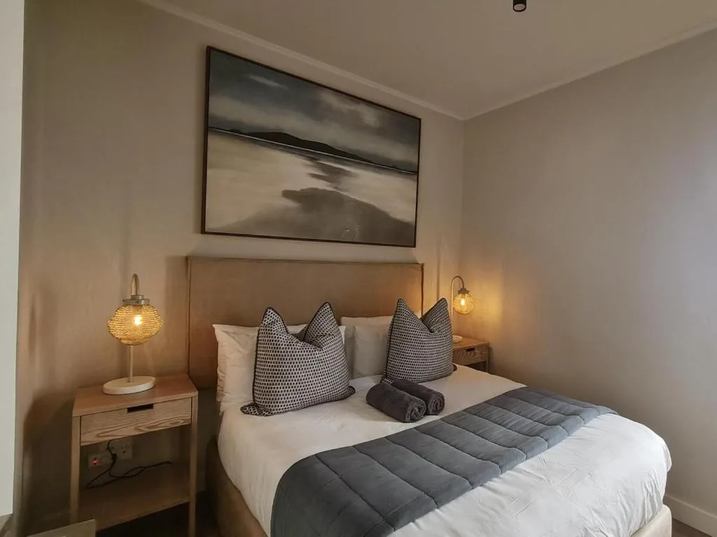 Modern bedroom with queen bed, patterned pillows, bedside lamps, and framed artwork