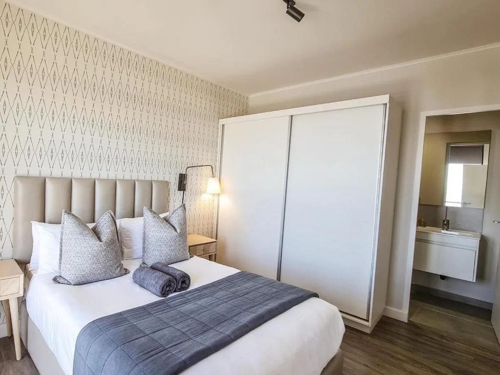 Modern bedroom with upholstered headboard, patterned wallpaper, and ensuite bathroom visible