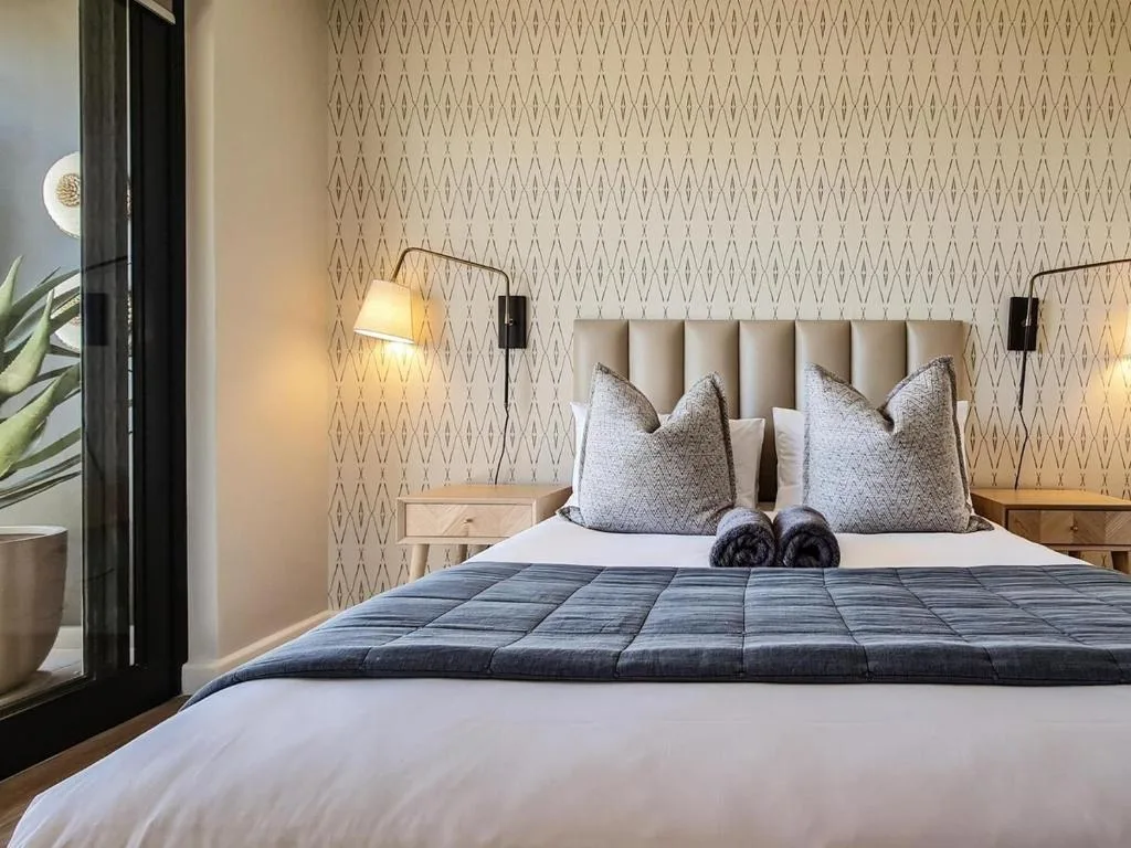 Modern bedroom with upholstered headboard, patterned wallpaper, and bedside lamps