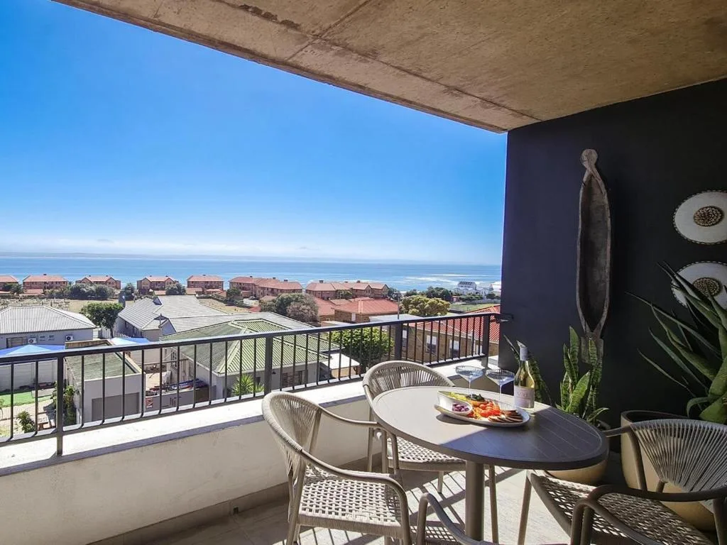 Elevated outdoor deck with dining table overlooking ocean and coastal neighborhood