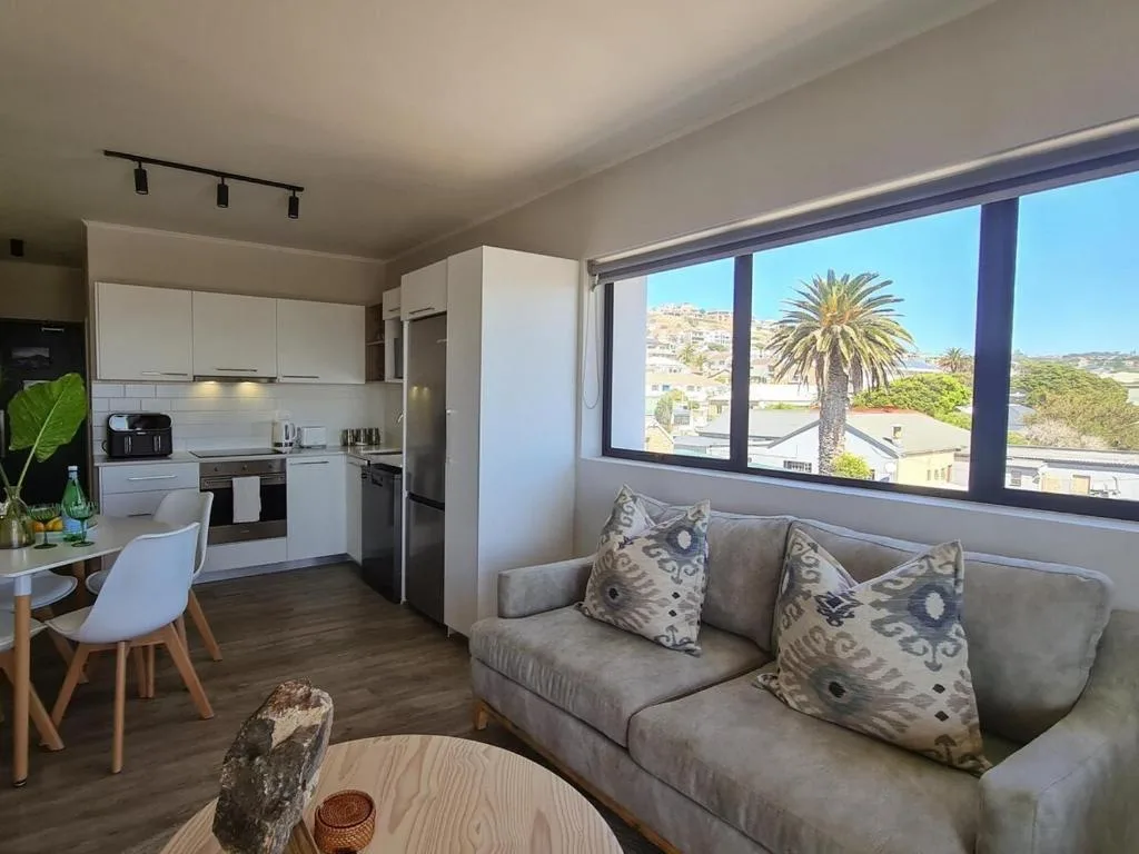 Modern lounge with sofa, kitchen visible, large windows overlooking palm tree and hills