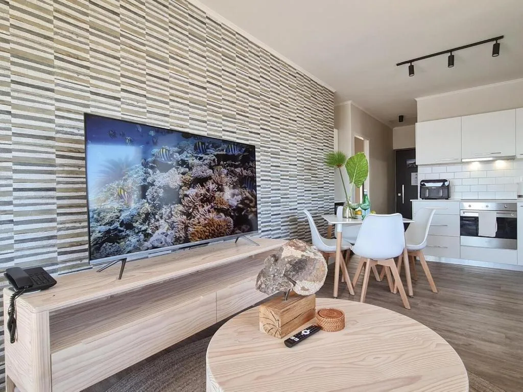 Modern lounge with TV, wooden furniture, and open kitchen view