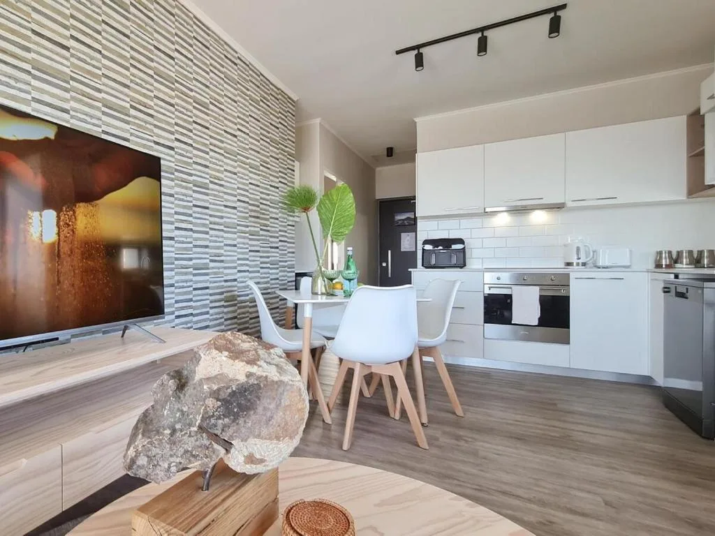 Modern open-plan lounge with TV, dining area, and kitchen beyond