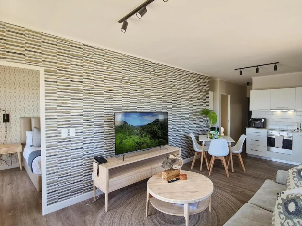 Modern open-plan lounge with TV, dining area, and kitchen visible in background