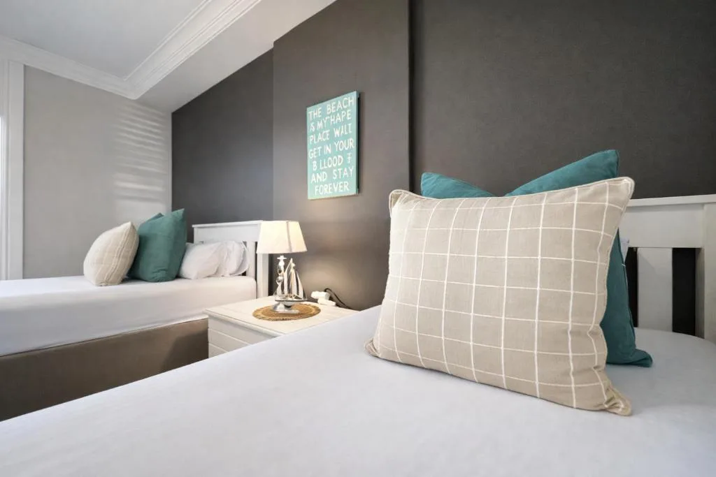 Modern bedroom with white bedding, teal accent pillows, and coastal wall art