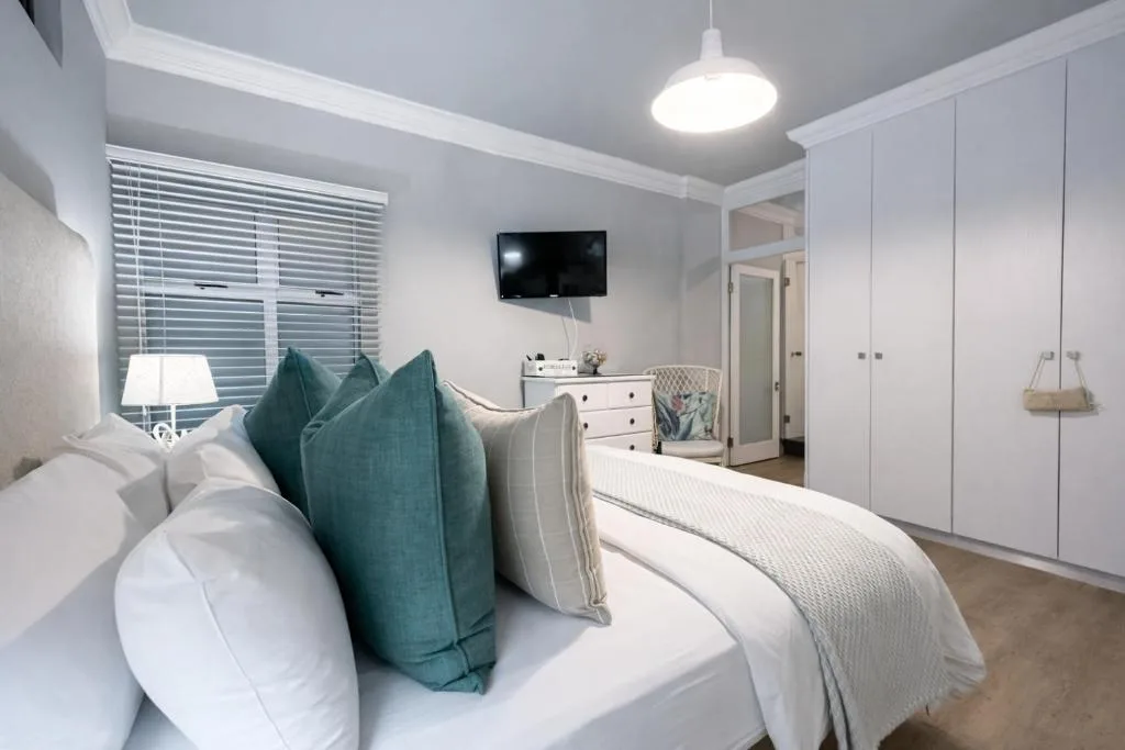 Bright modern bedroom with bed, teal pillows, TV, and built-in wardrobes