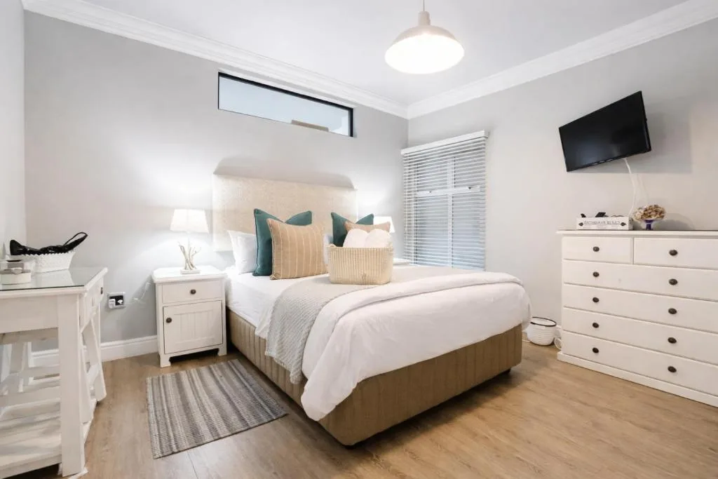 Bright bedroom with queen bed, white furniture, and wall-mounted TV