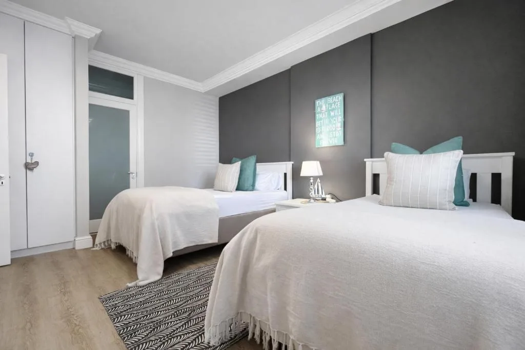 Modern bedroom with two twin beds, teal accents, and dark feature wall