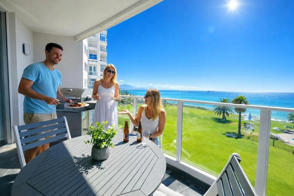 Family braaiing on oceanview balcony with turquoise sea and green lawns