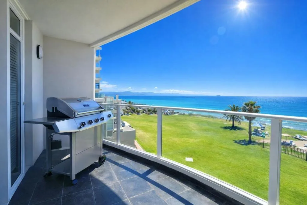 Outdoor balcony with braai grill overlooking turquoise ocean and manicured grounds