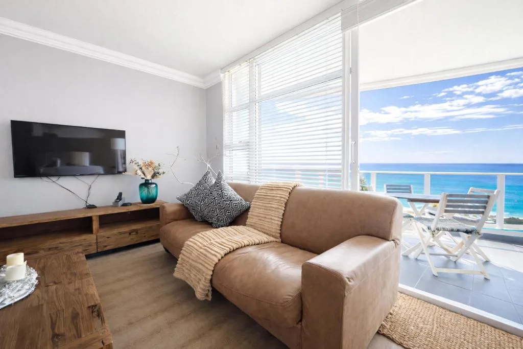 Bright lounge with beige armchair, TV, and ocean views through large windows