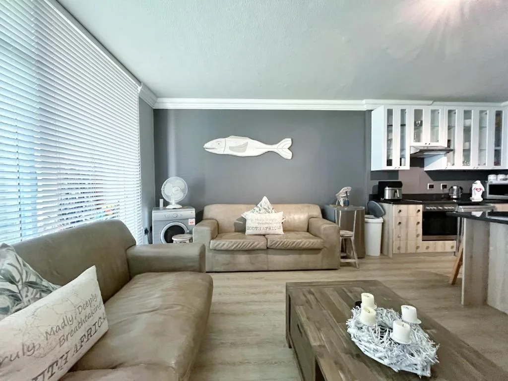 Open-plan living room with beige sofas, wooden table, and coastal decor