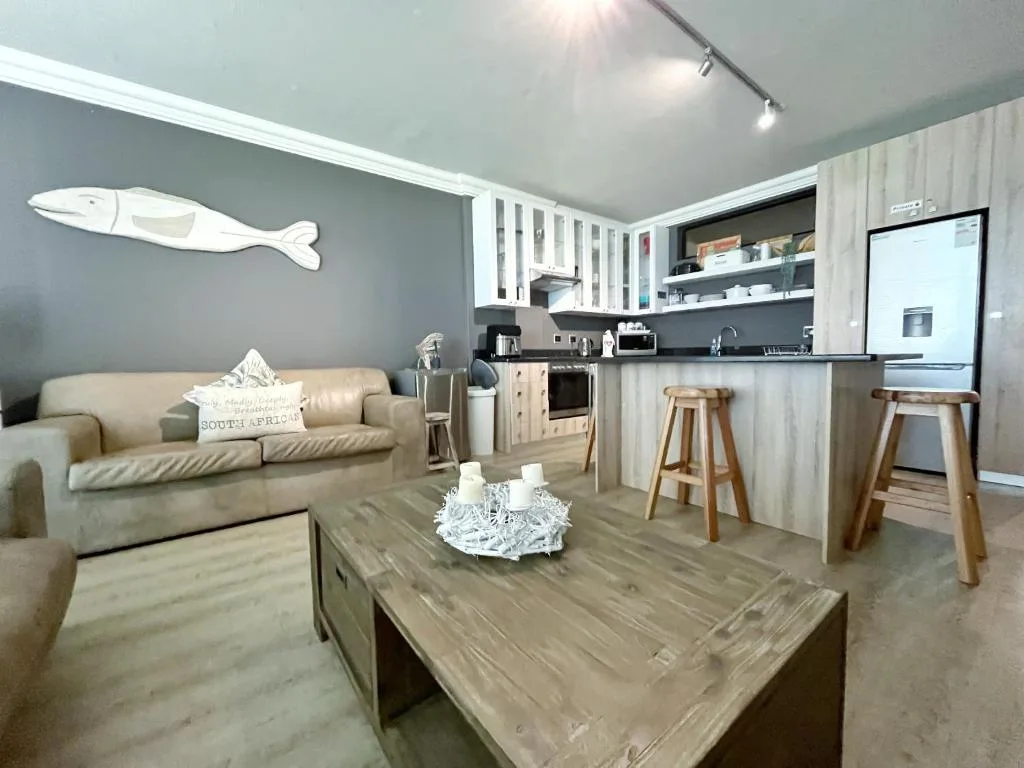 Open-plan lounge with beige sofa and wooden coffee table, kitchen visible beyond
